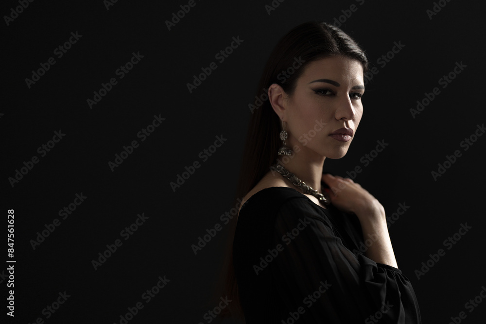 Naklejka premium An elegant, dressed-up woman showcasing a silver necklace and earrings, wearing a stylish black dress. Perfect for themes of fashion, elegance, and beauty.