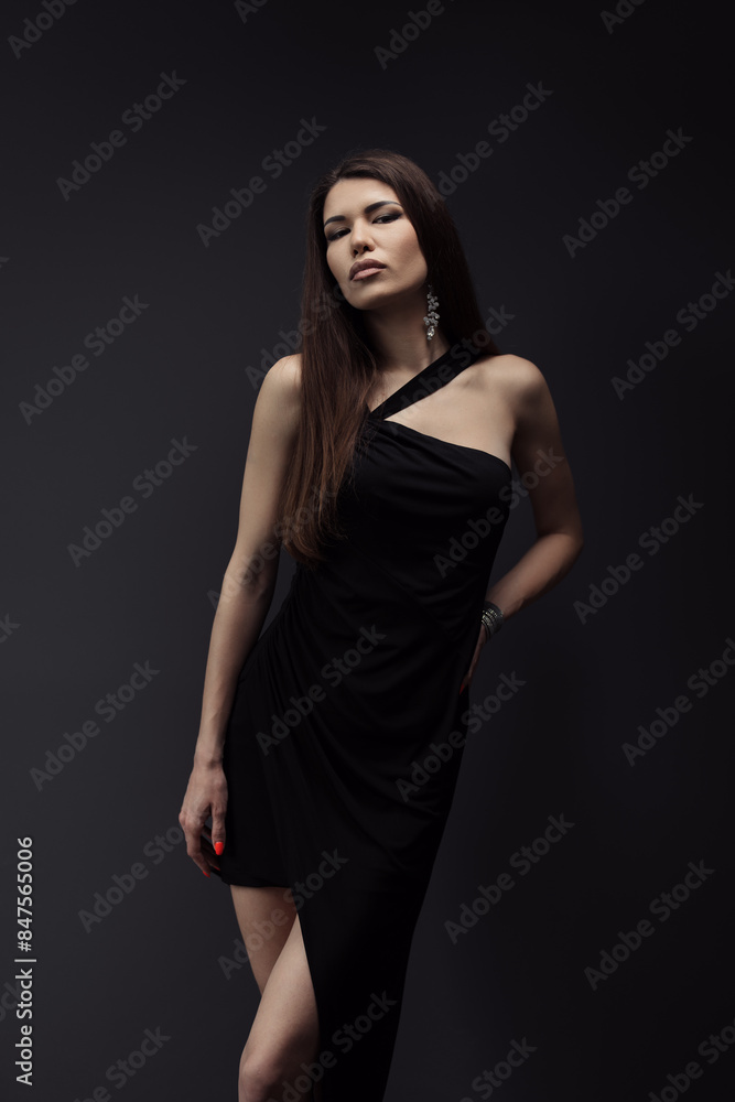 A sophisticated woman poses in a sleek black dress, exuding elegance and confidence against a dark studio backdrop. Perfect representation of fashion and style. A sophisticated woman poses in a sleek black dress, exuding elegance and confidence against a dark studio backdrop. Perfect representation of fashion and style.
