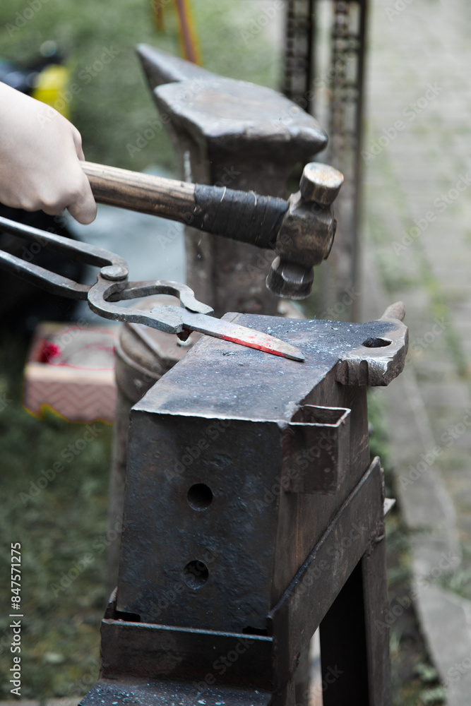 Teenager forging red hot steel with a hammer on an iron anvil . Close up view Teenager forging red hot steel with a hammer on an iron anvil . Close up view