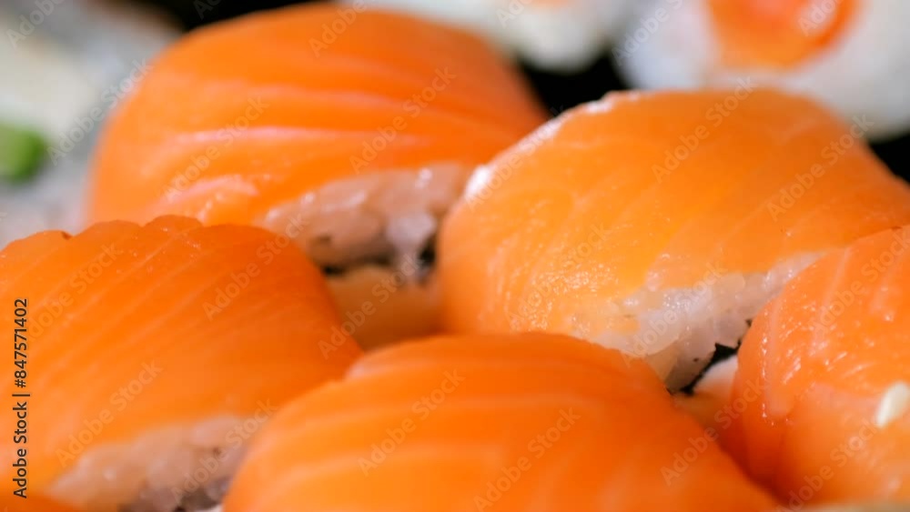 Sushi rolls set with tasty fresh salmon stripes on tray closeup. Asian dish with fish and rice served on plate. Gourmet food from Japanese restaurant Sushi rolls set with tasty fresh salmon stripes on tray closeup. Asian dish with fish and rice served on plate. Gourmet food from Japanese restaurant