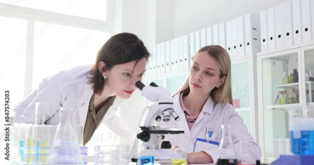Scientist invites colleague to look in microscope at sample Scientist invites colleague to look in microscope at sample