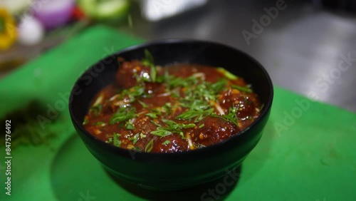 Garnishing green onions over the Manchurian balls with gravy in a bowl in India.	 photo