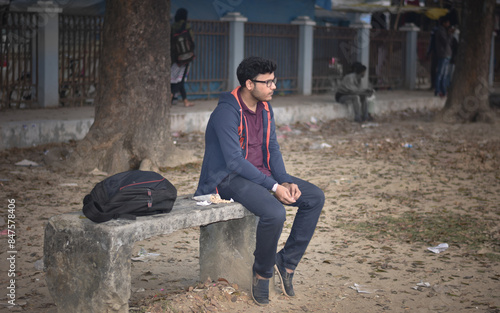 Asian Man in hoodie Sitting on a Bench in Urban Park of Bangladesh and eating Nuts.