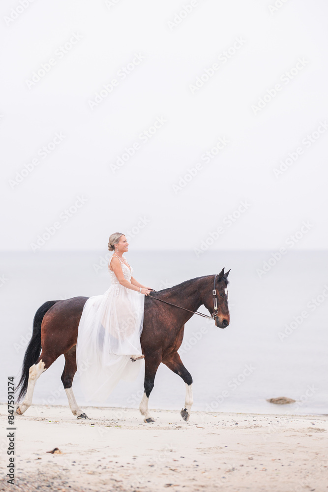 Bride in lace wedding dress riding a horse along the shoreline Bride in lace wedding dress riding a horse along the shoreline