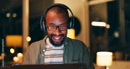 Night, headphones and black man in office with laptop for listening to music, album or playlist. Smile, creative and employee with computer for project deadline, proposal or feedback at design agency