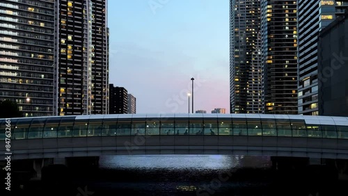 A pedestrian bridge illuminated at dusk between tall buildings in a cityscape