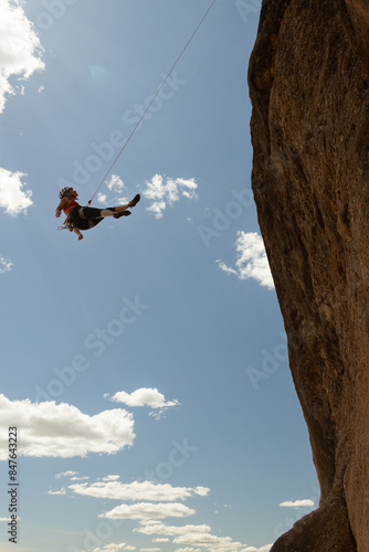 A woman is hanging from a rope on a cliff. Concept of adventure and excitement, as the woman is engaging in a thrilling activity. The white background adds a sense of contrast