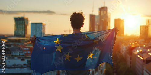 young man holding the European flag, with buildings in background, sunset light photo