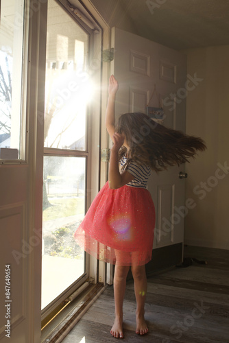 Side view of young girl twirling near sunny front door photo