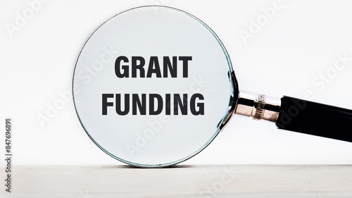 Business and grant funding concept. Copy space. Words GRANT FUNDING text appeared looking at a white background through a magnifying glass © Ihar