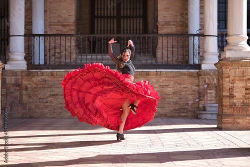 Young, beautiful, brunette woman in black shirt and red skirt, dancing flamenco between marble columns in Spain square in Seville. Flamenco concept, dance, art, typical Spanish.