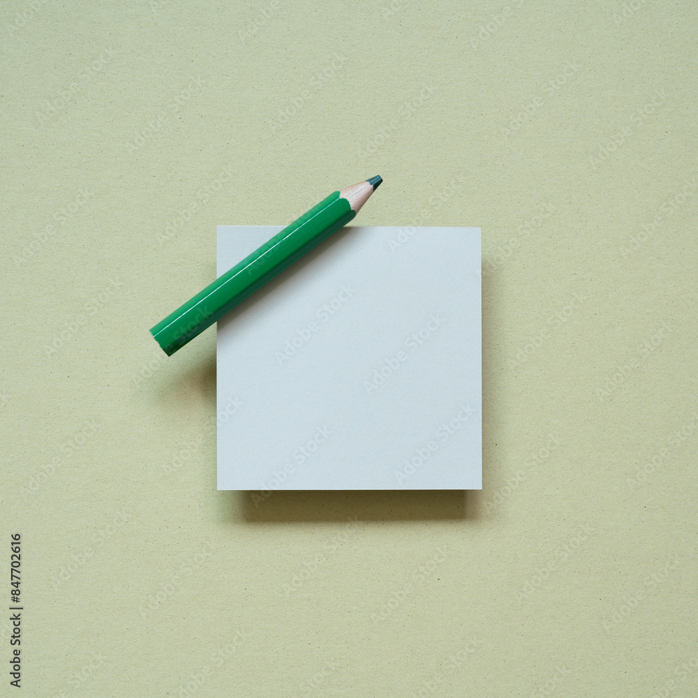 Blank memo pad with green pencil on khaki desk background. top view