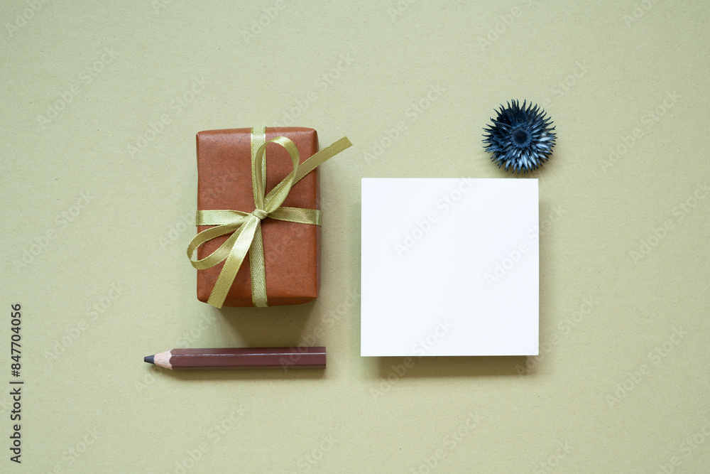 Brown gift box, colored pencil, memo pad, dry flower on khaki background. top view