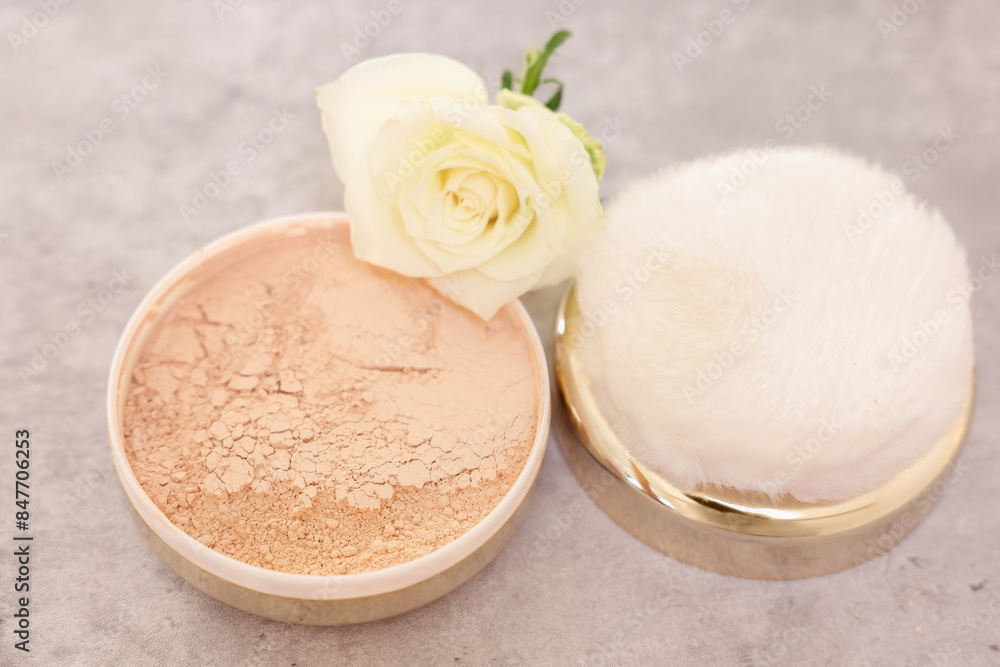 Face powder, puff applicator and rose flower on grey textured table, closeup Face powder, puff applicator and rose flower on grey textured table, closeup