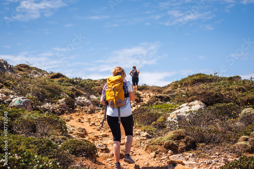 Two female hikers with backpack walking up to cliffs on Algarve coastline in Portugal. Active summer hiking vacation