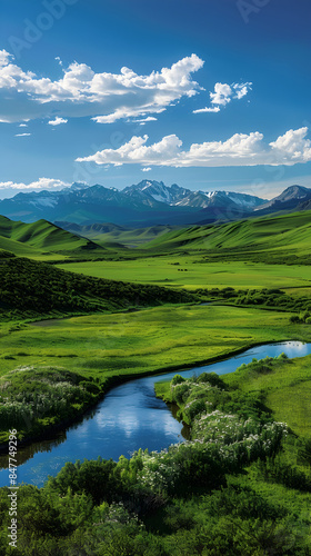 Serene Landscape with Rolling Hills, River, and Snow-Capped Mountains Under a Clear Blue Sky