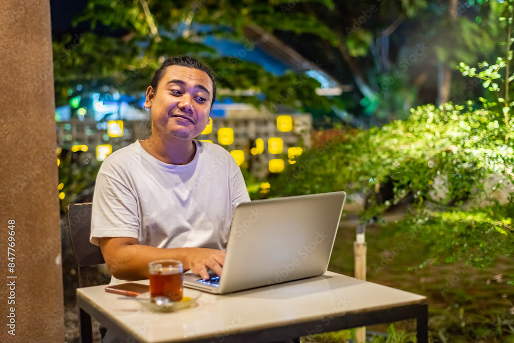 Young Asian man, digital nomad working remotely from cafe, using laptop and smartphone. young Asian men are hanging out in a cafe with a nature theme at night