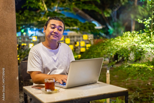 Obraz na płótnie Young Asian man, digital nomad working remotely from cafe, using laptop and smartphone. young Asian men are hanging out in a cafe with a nature theme at night w salonie