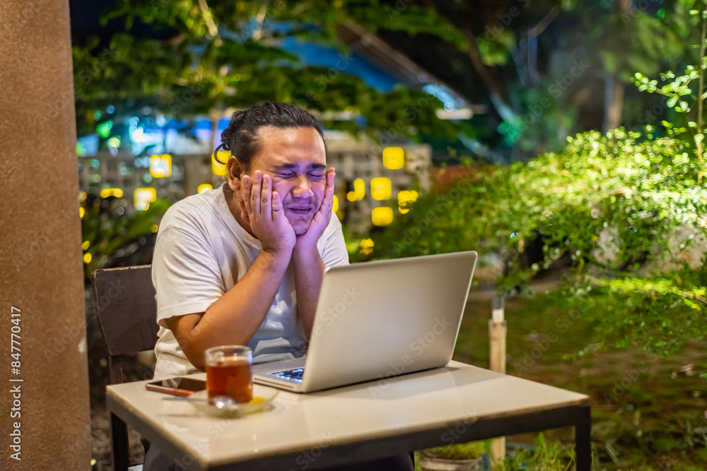 Young Asian man, digital nomad working remotely from cafe, using laptop and smartphone. young Asian men are hanging out in a cafe with a nature theme at night