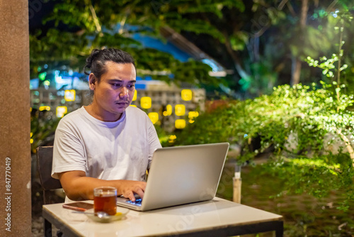 Obraz na płótnie Young Asian man, digital nomad working remotely from cafe, using laptop and smartphone. young Asian men are hanging out in a cafe with a nature theme at night w salonie