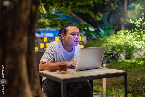 Young Asian man, digital nomad working remotely from cafe, using laptop and smartphone. young Asian men are hanging out in a cafe with a nature theme at night