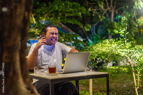 Obraz na płótnie Young Asian man, digital nomad working remotely from cafe, using laptop and smartphone. young Asian men are hanging out in a cafe with a nature theme at night w salonie