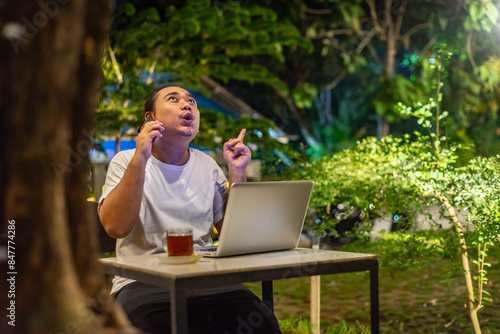 Obraz na płótnie Young Asian man, digital nomad working remotely from cafe, using laptop and smartphone. young Asian men are hanging out in a cafe with a nature theme at night w salonie