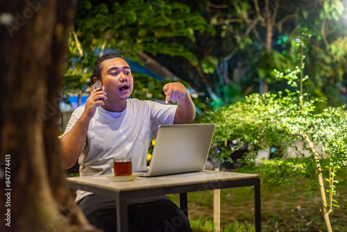 Obraz na płótnie Young Asian man, digital nomad working remotely from cafe, using laptop and smartphone. young Asian men are hanging out in a cafe with a nature theme at night w salonie