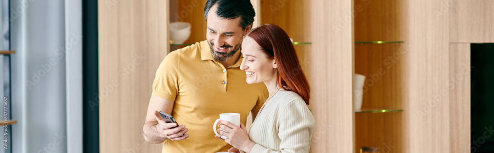 A bearded man and a redhead woman engrossed in their phone, sharing a moment of digital connection in their modern apartment. A bearded man and a redhead woman engrossed in their phone, sharing a moment of digital connection in their modern apartment.