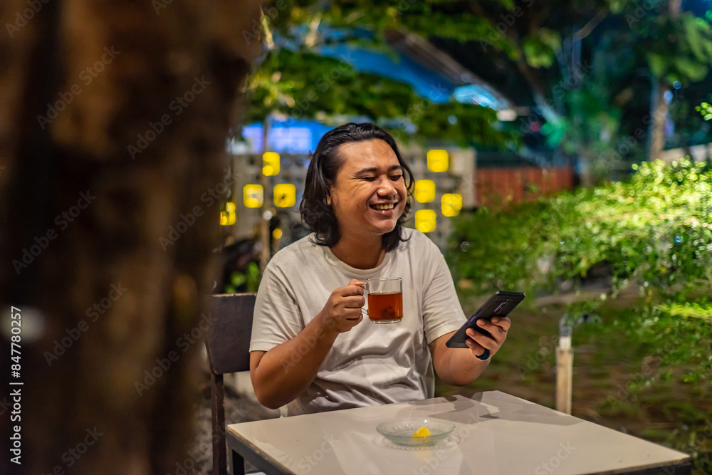 Young Asian man, digital nomad working remotely from cafe, using laptop and smartphone. young Asian men are hanging out in a cafe with a nature theme at night
