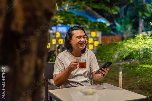 Obraz na płótnie Young Asian man, digital nomad working remotely from cafe, using laptop and smartphone. young Asian men are hanging out in a cafe with a nature theme at night w salonie