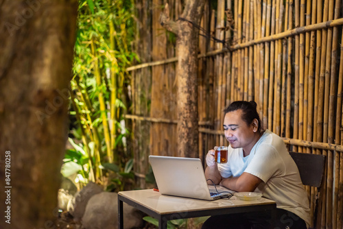 Obraz na płótnie Young Asian man, digital nomad working remotely from cafe, using laptop and smartphone. young Asian men are hanging out in a cafe with a nature theme at night w salonie