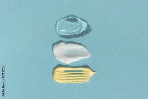 Smears of yellow, white cream and transparent gel or serum on a blue background. The texture of a cosmetic skin care product. Top view.