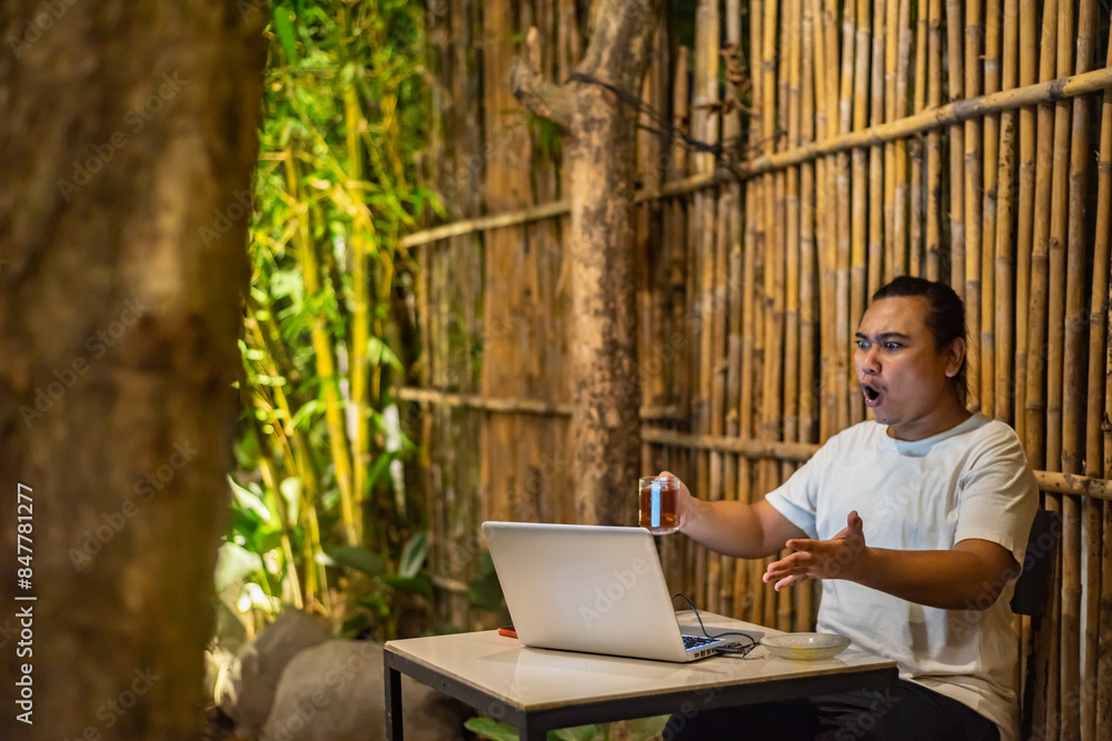 Young Asian man, digital nomad working remotely from cafe, using laptop and smartphone. young Asian men are hanging out in a cafe with a nature theme at night