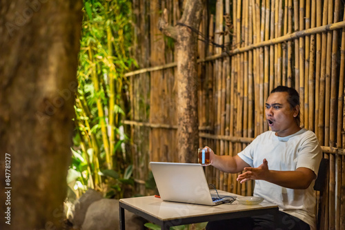 Obraz na płótnie Young Asian man, digital nomad working remotely from cafe, using laptop and smartphone. young Asian men are hanging out in a cafe with a nature theme at night w salonie