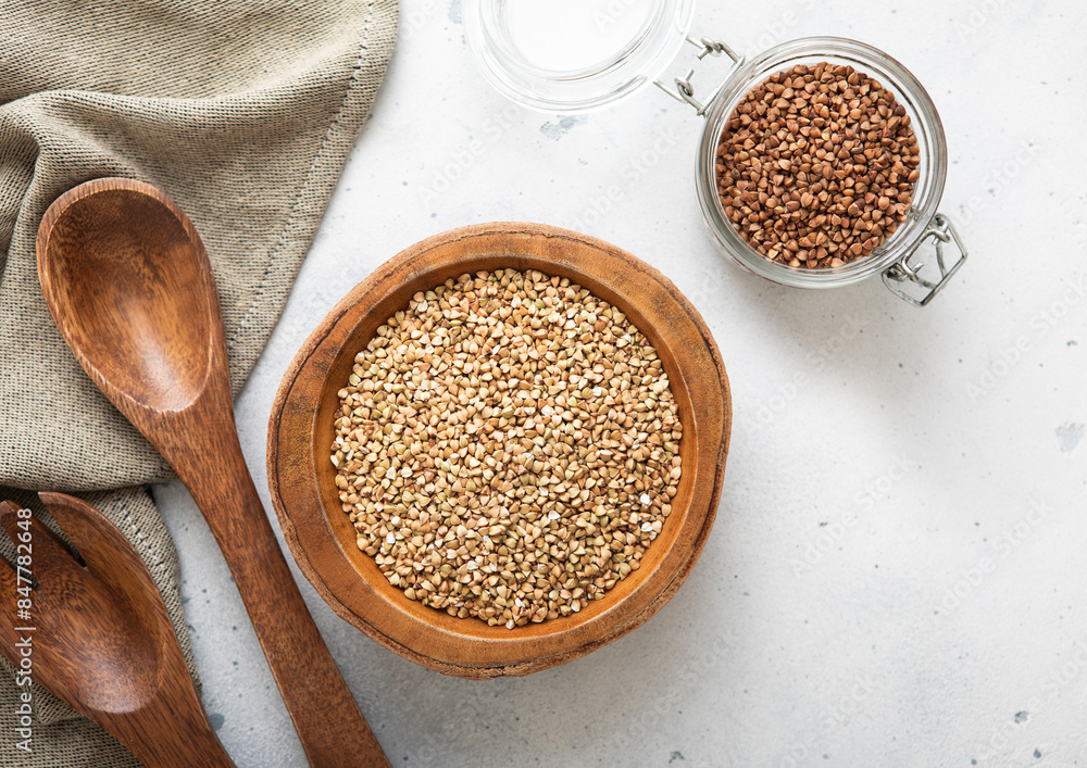 Bowl of green dry raw organic buckwheat seeds on light table with kitchen wooden spoon.Macro. Bowl of green dry raw organic buckwheat seeds on light table with kitchen wooden spoon.Macro.