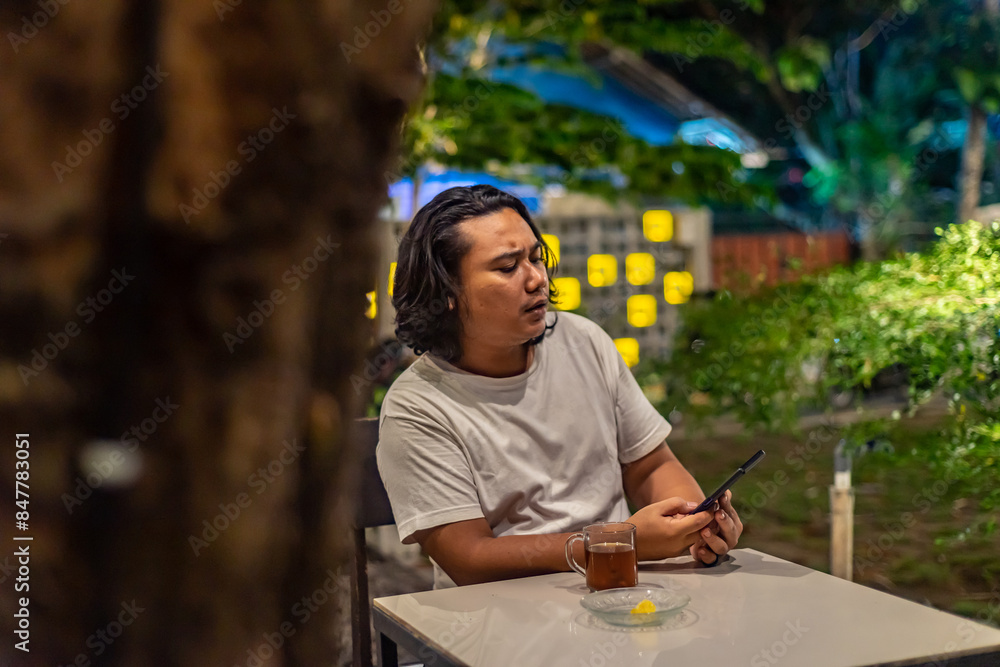 Young Asian man, digital nomad working remotely from cafe, using laptop and smartphone. young Asian men are hanging out in a cafe with a nature theme at night
