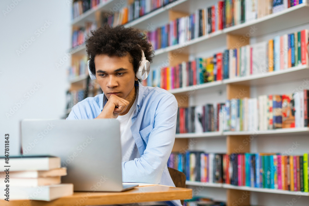 Focused sad latin student guy sitting in front of laptop in university library, poignant scene capturing the challenges and fatigue of academic endeavors Focused sad latin student guy sitting in front of laptop in university library, poignant scene capturing the challenges and fatigue of academic endeavors