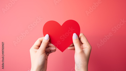 Hands holding blank paper greeting or invitation card over red background with heart shape. Christmas, Valentine day, New Year, winter holidays concept.