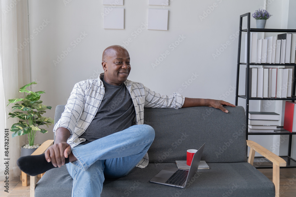 Fototapeta premium Portrait of happy African American small business owner. Millennial black smiling, sitting and using the laptop, and holding a cup of coffee work in modern office.