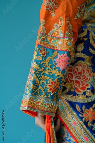Close-up of a bright, colorful, traditional Asian garment sleeve with intricate floral embroidery, set against a blue background.