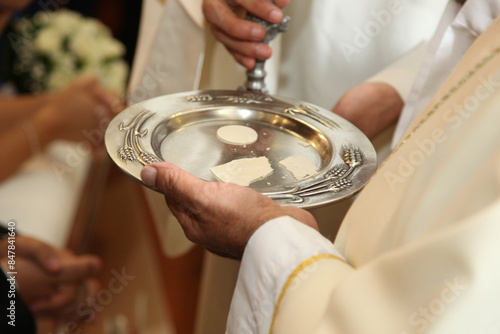 Принти на полотні Priest holding a metal paten with consecrated hosts during a church service