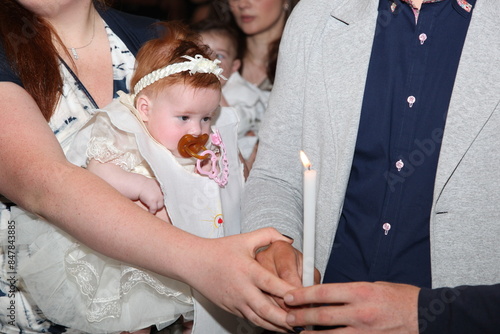 Parents holding a white burning candle with their baby girl during a baptism ceremony in a church photo