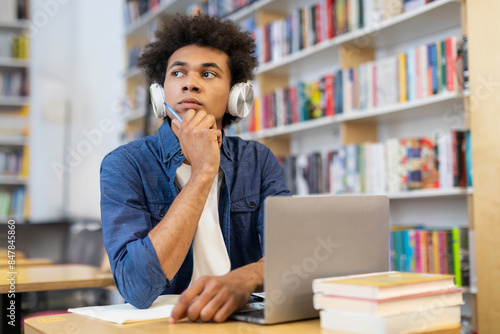 фотографія Pensive African American male student in headphones looking away, creating essay