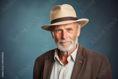 Portrait of a grinning man in his 60s donning a classic fedora while standing against pastel or soft colors background