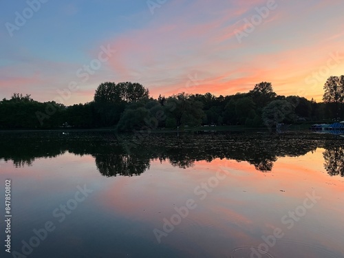 Purple sky reflection on the water surface, lake in park, silhouettes of the trees reflection 