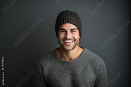 Portrait of a grinning man in his 30s donning a warm wool beanie in front of minimalist or empty room background