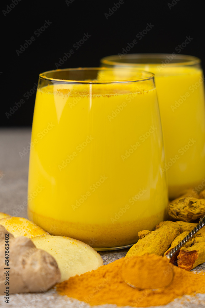 Golden milk, a traditional Ayurvedic drink with turmeric in two glasses on a black gray background Golden milk, a traditional Ayurvedic drink with turmeric in two glasses on a black gray background