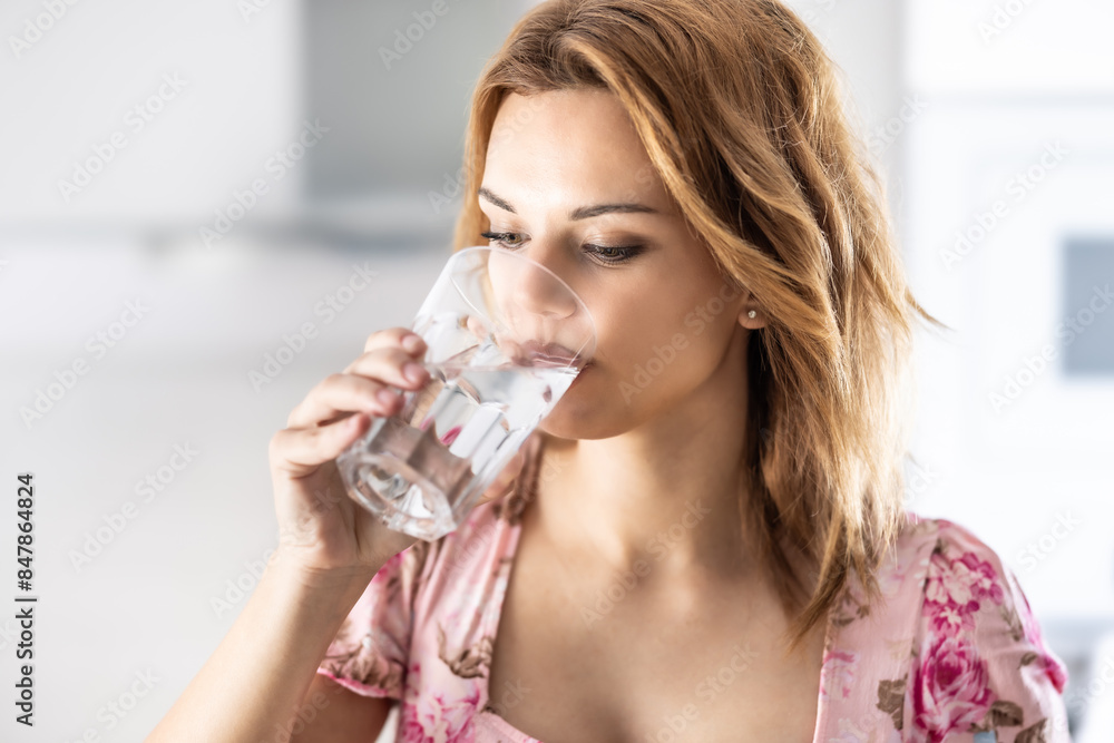Young cute woman drinking pure water from glass in her kitchen Young cute woman drinking pure water from glass in her kitchen