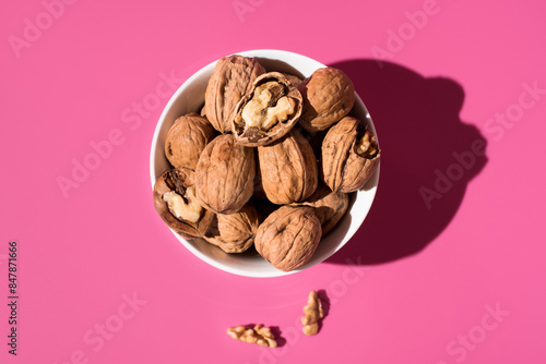 Nueces doradas en un recipiente blanco sobre fondo rosa. Vista superior	